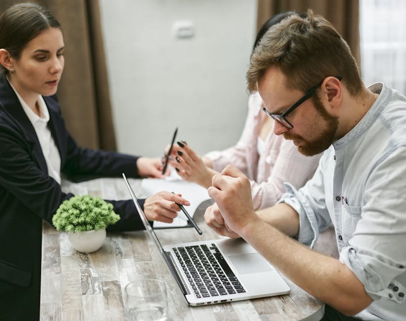 Three professionals engage in a collaborative meeting, discussing ideas over a laptop in an office setting.